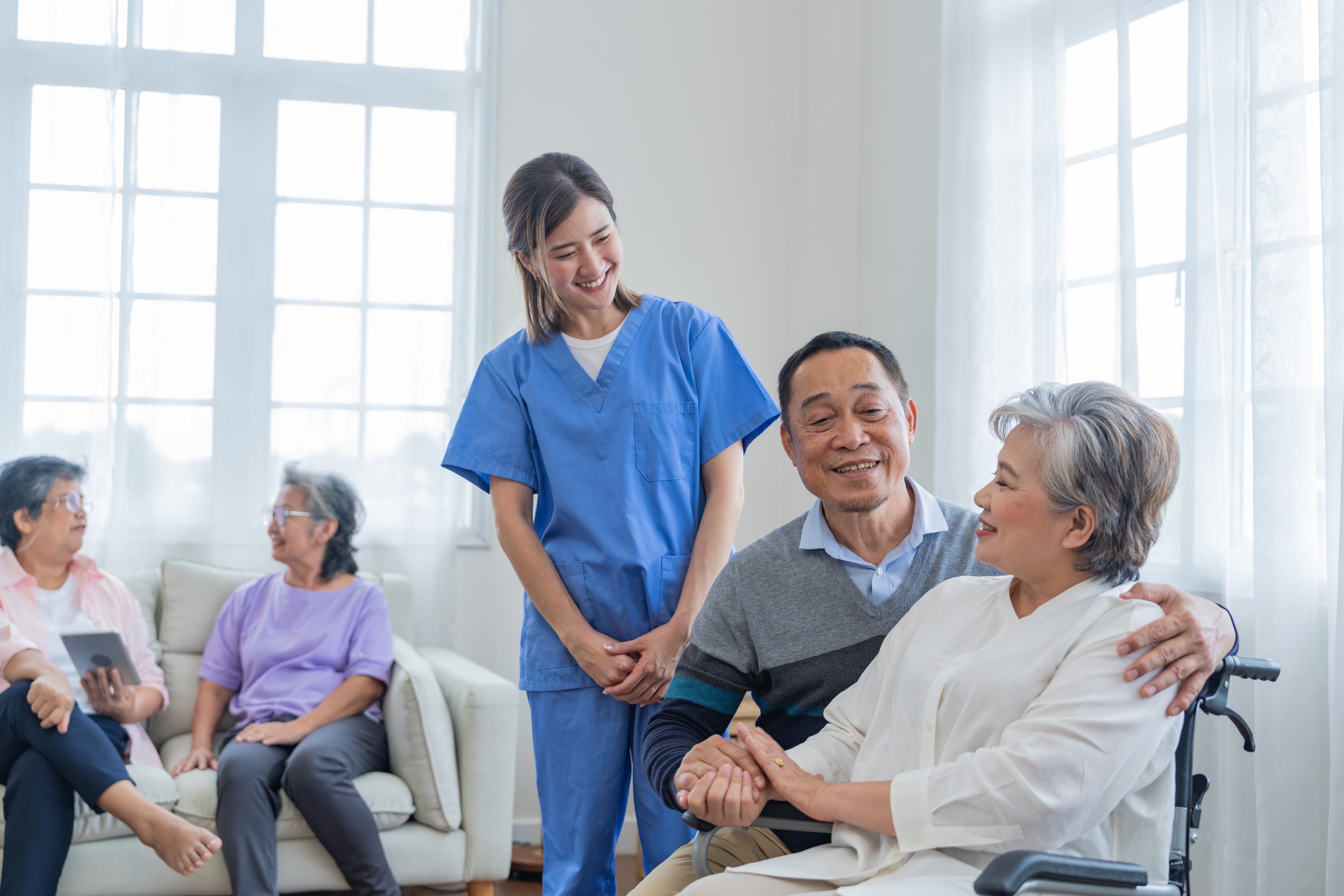 Hospice Palliative Review is Now Part of BoardCerts, Inc. Smiling caregiver with a senior couple in a bright care setting
